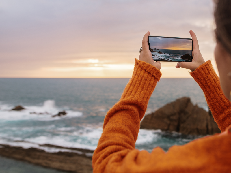 person in amaysim coloured jumper photographing the ocean with an iPhone 14 pro